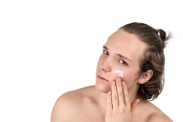 Knappe jonge shirtless man het aanbrengen van crème op zijn gezicht op witte achtergrond geïsoleerd. Mannen gezondheid en huidverzorging — Stockfoto