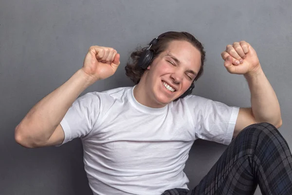 Bonito jovem sentado no chão na sala de estar, com fones de ouvido na cabeça e ouvindo música — Fotografia de Stock