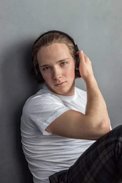 Snygg ung man sitter på golvet i vardagsrummet, med hörlurar på huvudet och lyssnar musik — Stockfoto