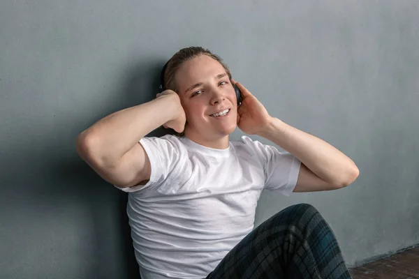 Pohledný mladý muž, který sedí na podlaze v obývacím pokoji, má sluchátka na hlavě a poslouchá hudbu — Stock fotografie