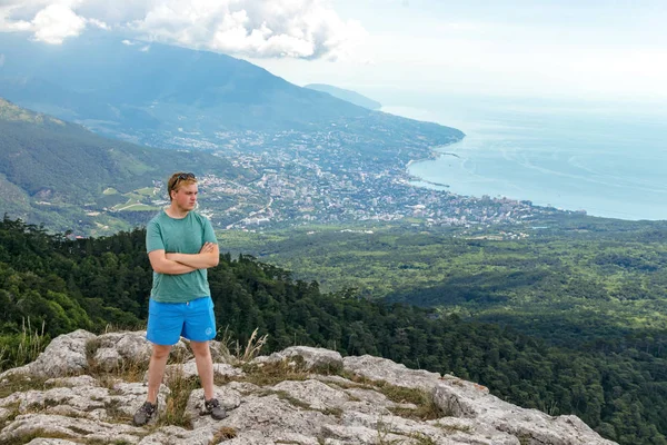 Joven hombre de pie en la cima del acantilado en las montañas y disfrutar de la vista de la naturaleza. Montañas y mar —  Fotos de Stock