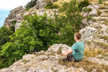Yoga yapan genç adam kayalık tepede otururken poz veriyor. Adam meditasyon yapmak ve manzaranın tadını çıkarın