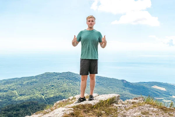 Joven hombre de pie en la cima del acantilado en las montañas y disfrutar de la vista de la naturaleza. Montañas y mar —  Fotos de Stock