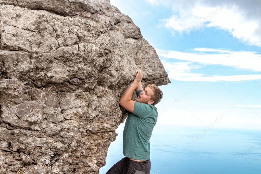 Young man hanging on edge, climbs up the rock