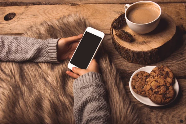 white phone in the hands of the girl, coffee cookies, cones and fur