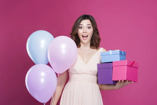 Chica en un vestido, se sorprende y tiene regalos en la mano, sobre un fondo rosa — Foto de Stock