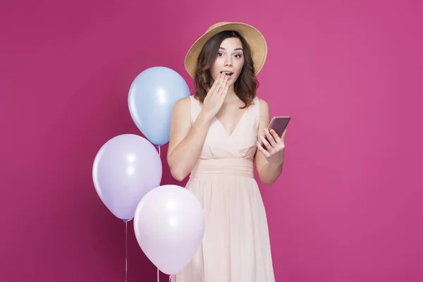 Chica sorprendida con un teléfono en sus manos sobre un fondo rosa — Foto de Stock