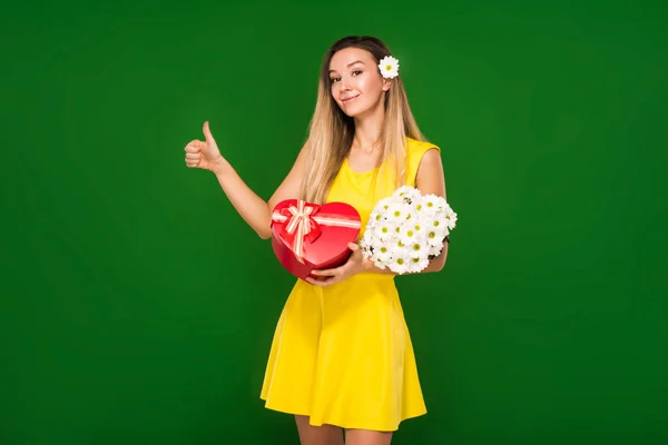 Chica rubia en un vestido amarillo sostiene un ramo de manzanillas y una caja de regalo — Foto de Stock