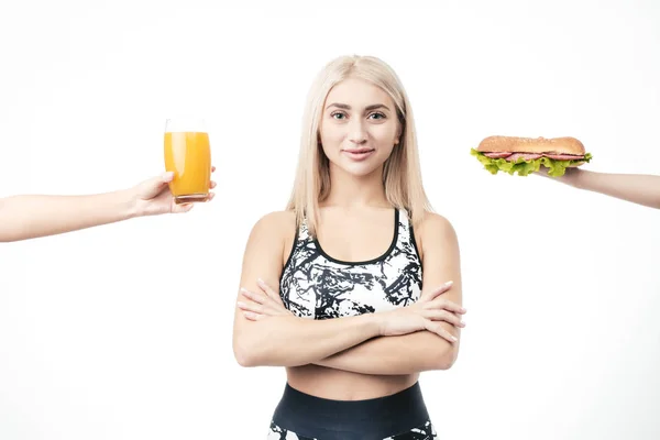 Sportieve blonde houdt in haar hand, een hamburger en een glas verse jus — Stockfoto