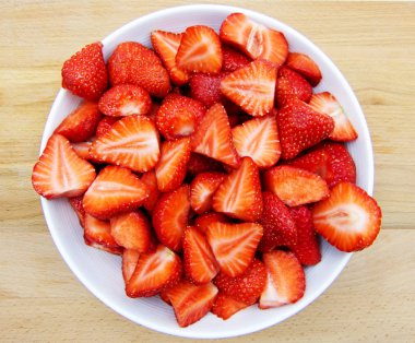 Ahşap masa üzerinde beyaz bir tabak üzerinde dilimlenmiş çilek