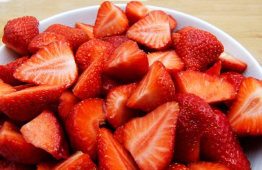 Ahşap masa üzerinde beyaz bir tabak üzerinde dilimlenmiş çilek