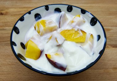 Ahşap arka planda şeftali dilimleri olan bir kasede yoğurt.