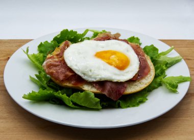 Beyaz çanak, ahşap masa üzerinde ekmek, jambon ve salata ile kızarmış yumurta