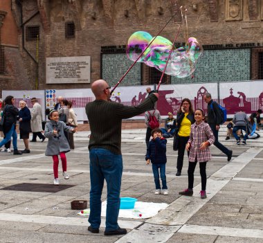 Bolonya / İtalya - 12 Ekim 2019: Sokak sanatçısı İtalya 'nın Bologna kentindeki Piazza del Nettuno' da büyük sabun köpükleri yapıyor. Çocuklar onun etrafında mutlu bir şekilde toplanıyor..