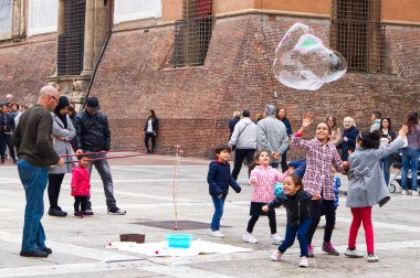 Bolonya / İtalya - 12 Ekim 2019: Sokak sanatçısı İtalya 'nın Bologna kentindeki Piazza del Nettuno' da büyük sabun köpükleri yapıyor. Çocuklar onun etrafında mutlu bir şekilde toplanıyor..