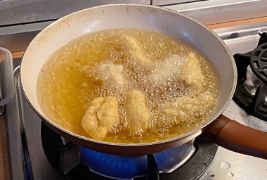 Delicious pieces of food are actively deep frying in hot bubbling oil on a gas stove in a home kitchen.