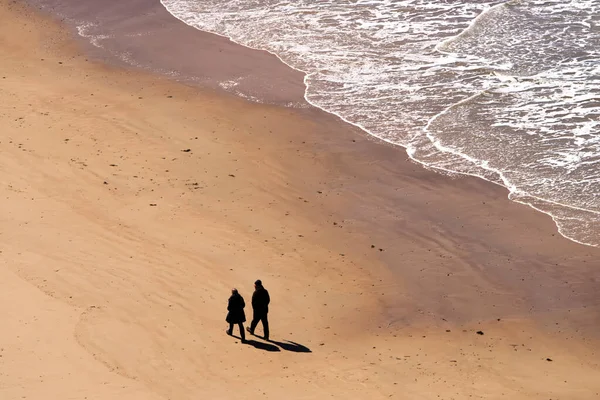 Two people are walking on the beach