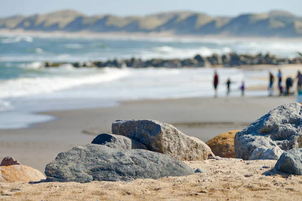前景の大きな石や背景のぼやけたビーチの風景や人々 — ストック写真