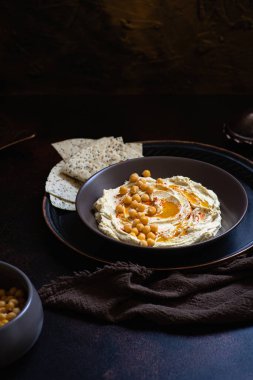 Humus - nohut sosu - seramik bir kasede servis edilir, koyu renkli arka planda füme paprika ve pita ekmeği ile. Yakın çekim, seçici odak, kopyalama alanı