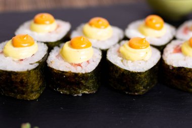 Kompozisyonda siyah bir taş üzerinde suşi ve rulo