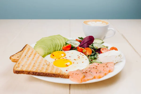 Fried eggs with toast, salad, cheese, salmon and avocado, breakfast