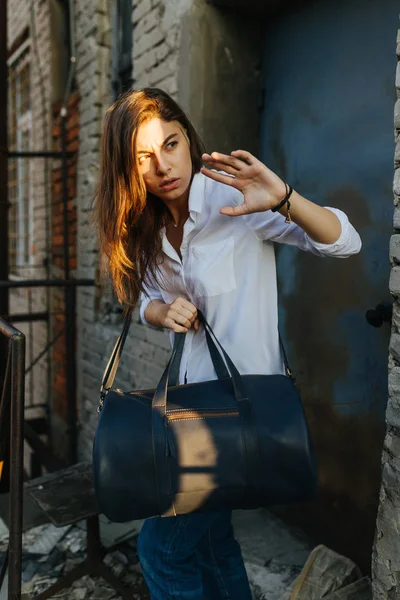 Girl with a leather bag in the city among the brick walls