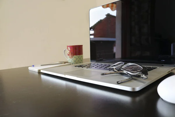 Office objects composition, Black desk, laptop, mouse, breakfast cup, sketch pad, pen, eyeglasses