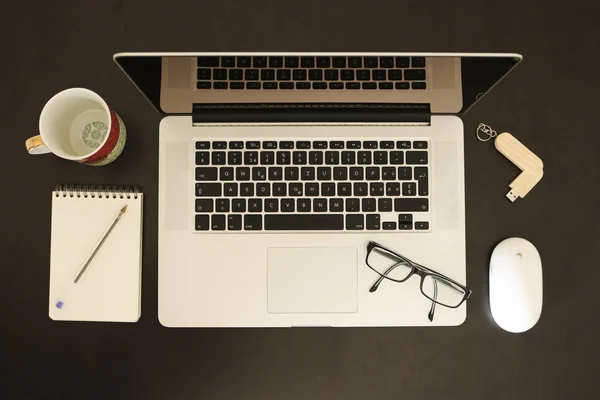Office objects composition, Black desk, laptop, mouse, USB flash drive, breakfast mug, sketch pad, pen, eyeglasses, top view