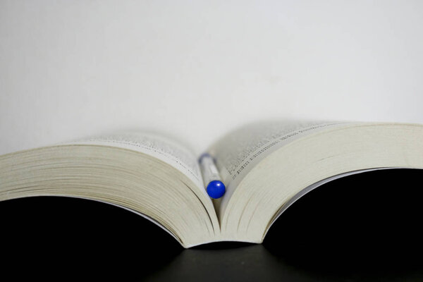 Крупный план открытой книги литературы и ручки между страницами на белом фоне
