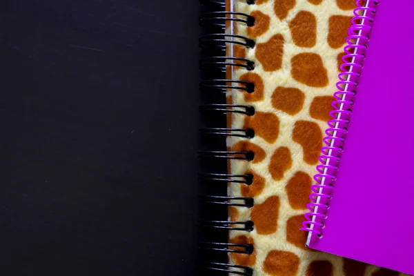 Detail of a leopard-print notebook and pink notebook with the black background viewed from above, office objects