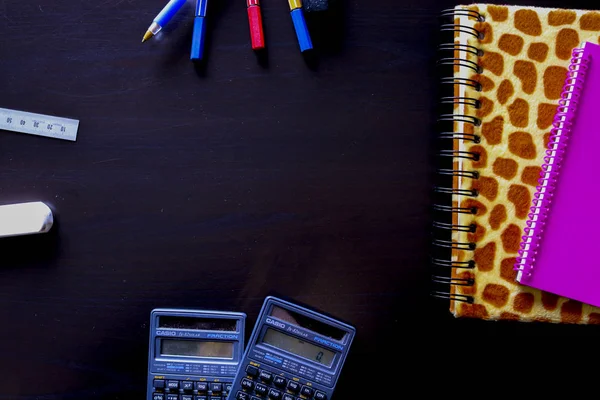 Composition of office objects composed of two notebooks with two calculators, pens and a highlighter on a black background viewed from above