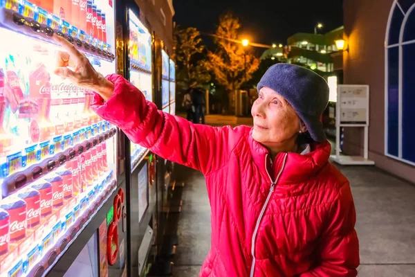 Oidentifierad äldre kvinna köper en flaska vatten från en automat — Stockfoto