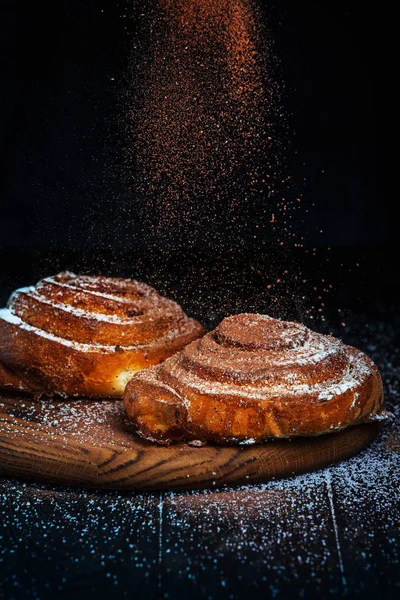 Homemade cinnamon buns with powdered sugar. Concept of action low key food photography. Flying sugar, freeze motion. Free copy space for text, logo, brand. Homemade bakery.