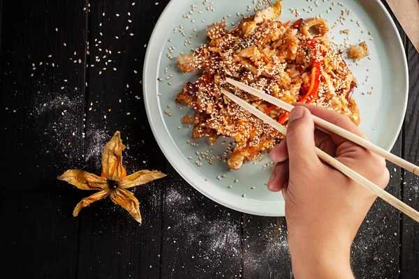 Man\'s hand holds chopsticks to eat Chinese rice with chicken. Asian fastfood. Chinese cuisine, close up view, top view food, copy space for text.