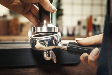 Barista presses ground coffee using tamper. Toned picture. Close up view of barista work. Copy space for text, logo or brand clipart