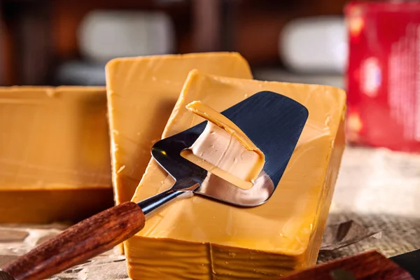 Block of Traditional Norwegian sweet brown cheese and cheese cutter. Gudbrandsdalsost. Close up view. Copy space for text, logo or brand. Delicious cheese on wooden table in shop.