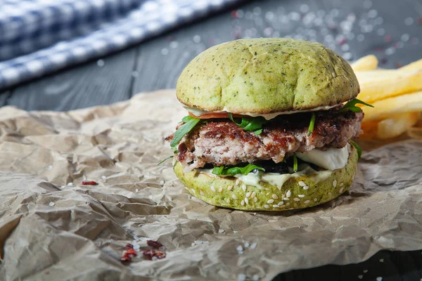 Burger with meat, sauce, salt and vegetables on craft paper. Snack with a green bun on a dark wooden background with insta tint. Close up view on american fast-food. Copy free space for logo, text
