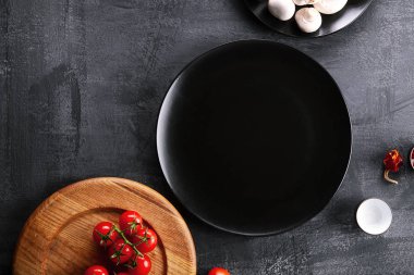 Boş gıda sofra ahşap kesme tahtası aletleri ve koyu arka plan üzerinde siyah plaka. Restoran, yemek menüsü, Cafe konsept. Ücretsiz kopya alanı. Kiraz domates, yemek pişirmek için mashrooms maddeler. Üstten görünüm