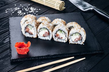 Suşi rulo siyah taş çubuklarla servis. Suşi koyu arka plan üzerinde görünümü kapatın. Geleneksel Japon mutfağı. Restoran, yemek menüsü, yemek tarifi, Cafe konsept. Kopya alanı sayesinde Live tarzı
