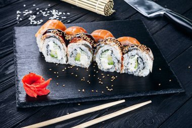 Suşi rulo siyah taş çubuklarla servis. Suşi koyu arka plan üzerinde görünümü kapatın. Geleneksel Japon mutfağı. Restoran, yemek menüsü, yemek tarifi, Cafe konsept. Kopya alanı sayesinde Live tarzı