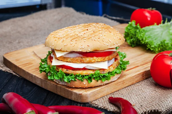 Double Chicken Burger with meat, sauce and vegetables on on wooden background. Close up view on american fast food. Restaurant, food menu, recipe, cafe concept. Lifestyle with copy space