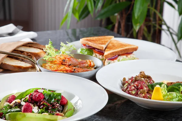 Close up view on table with plenty of food. European and Middle Eastern cuisine. Food for lunch. Srimp, tartare salad and toast on marble table. Set of dishes lunch on table concept with copy space.