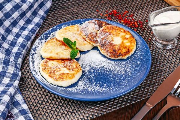 Traditional homemade ukrainian cheese pancake with sour cream on blue plate. Ukrainian cuisine. Restaurant, food menu, recipe, cafe concept. Free copy space for text. Close up cheese pancake dessert