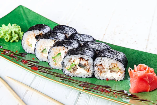 Spice Maki rolls with eel on green plate served with ginger and wasabi on white wooden table. Fresh Japanese cuisine. Close up view on asian food. Sushi image for menu.