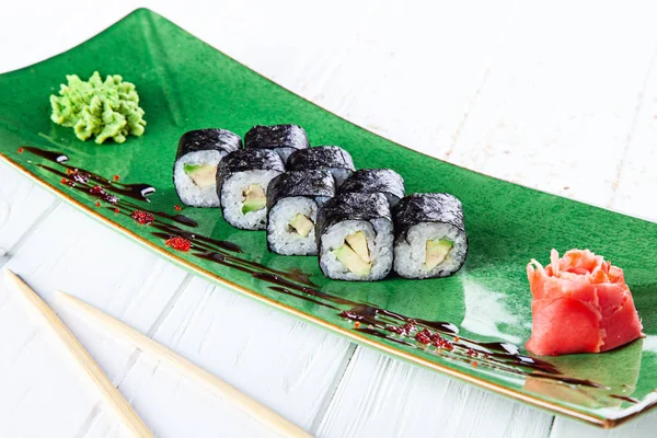 Maki rolls with avocado on green plate served with ginger and wasabi on white wooden table. Fresh Japanese cuisine. Close up view on asian food. Sushi image for menu.