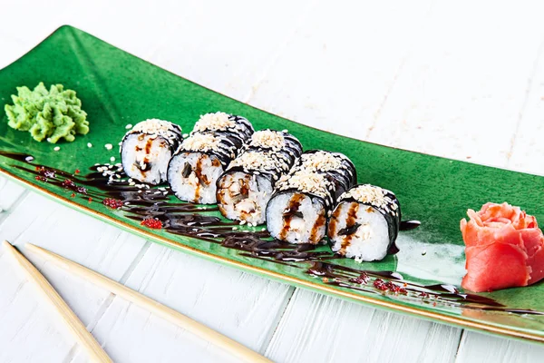 Maki rolls with eel on green plate served with ginger and wasabi on white wooden table. Fresh Japanese cuisine. Close up view on asian food. Sushi image for menu.