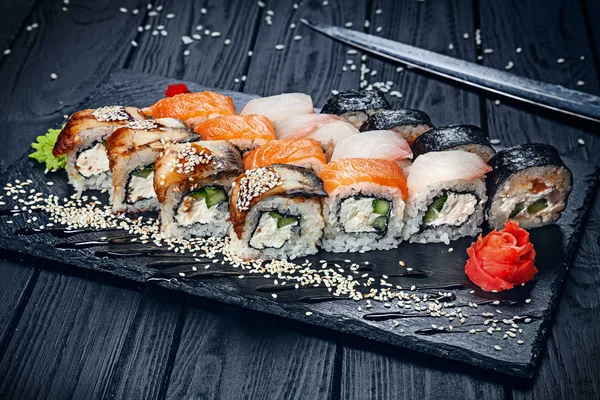 A set of sushi rolls with salmon on dark stone served with ginger and wasabi and wooden black wooden table. Fresh Japanese cuisine. Close up view on asian food. Sushi image for menu.