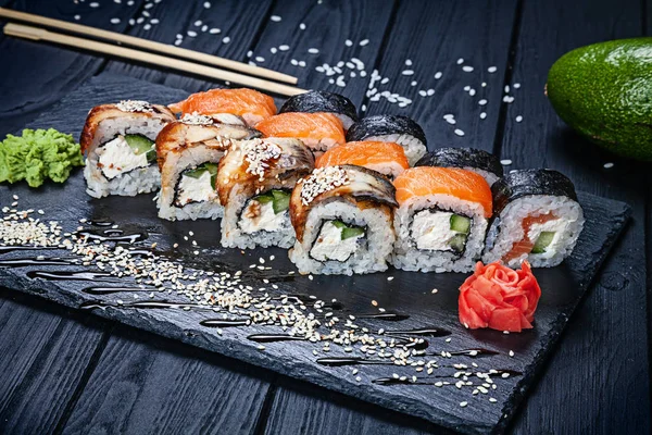 A set of sushi rolls with salmon on dark stone served with ginger and wasabi and wooden black wooden table. Fresh Japanese cuisine. Close up view on asian food. Sushi image for menu.