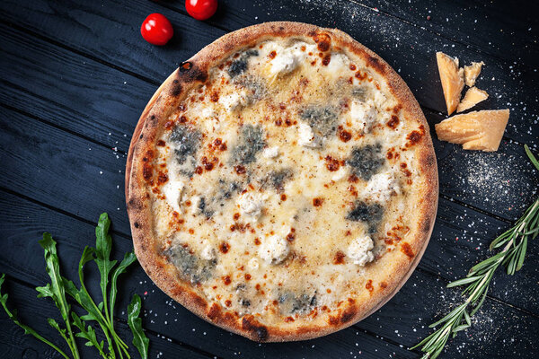 Top view on fresh homemade italian four chees pizza. Pizza, cheese, cherry tomato and parsley on dark wooden background with copy space for design. Pizza made of corn flour. Top view food menu, recipe