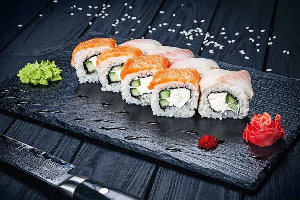 Set of sushi rolls with salmon on dark stone served with ginger and wasabi and wooden black wooden table. Fresh Japanese cuisine. Close up view on asian food. Sushi image for menu.